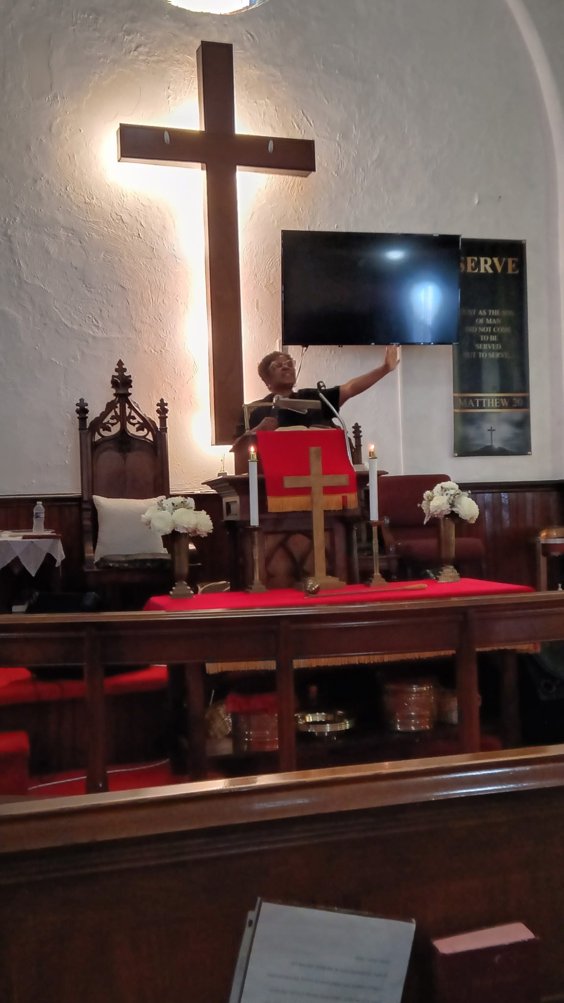 Rev. Angela Brown-Vann preaching from the pulpit at Alleyne Memorial, with the illuminated cross behind her